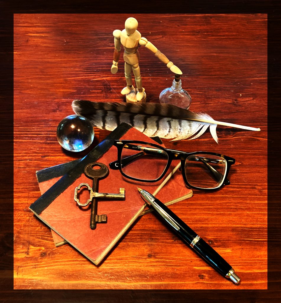 Photo of human figurine, glass bottle, feather, glass ball, books, glasses, keys and pen