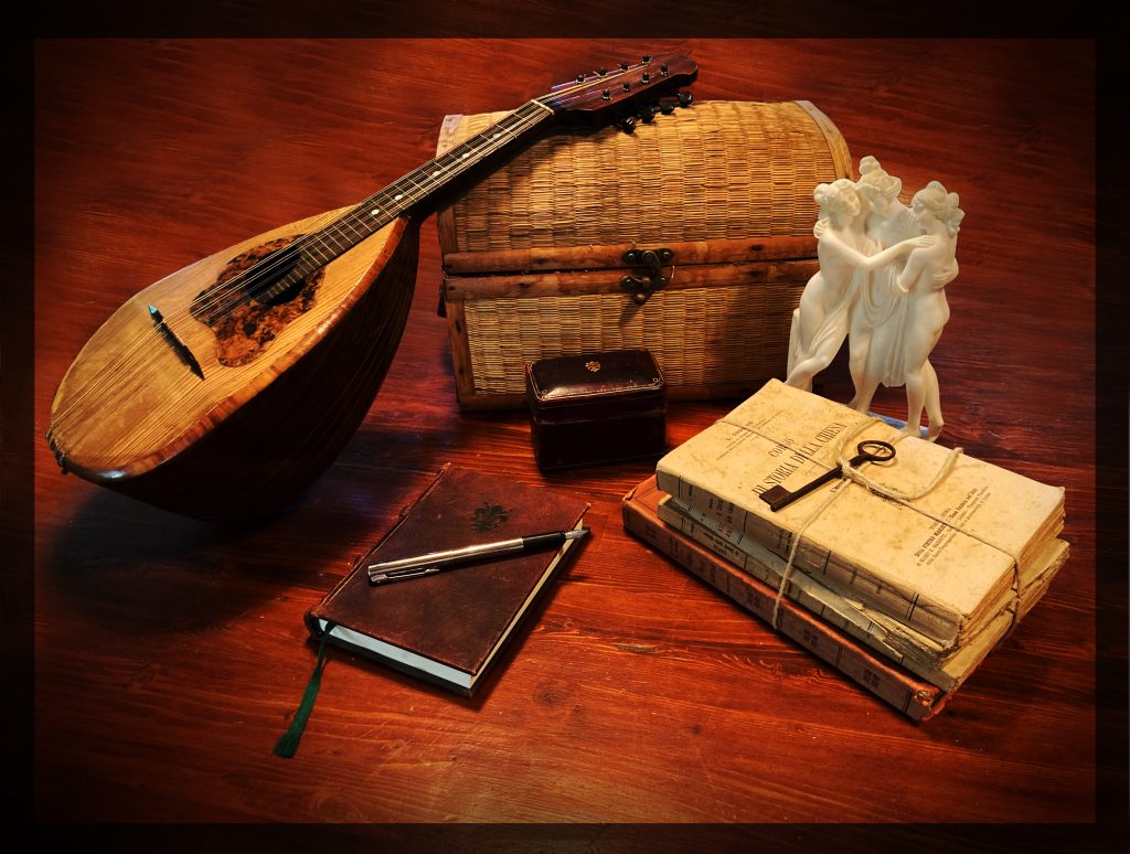 Photo still life of mandolin, wicker chest, books, pen, statue and key.